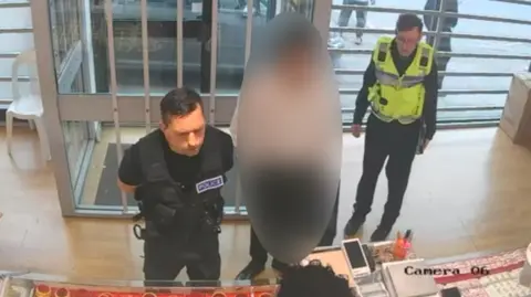 CCTV footage of two men dressed in police uniform at a custody desk.