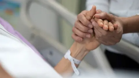 Hospital visitor holds the hand of a patient.