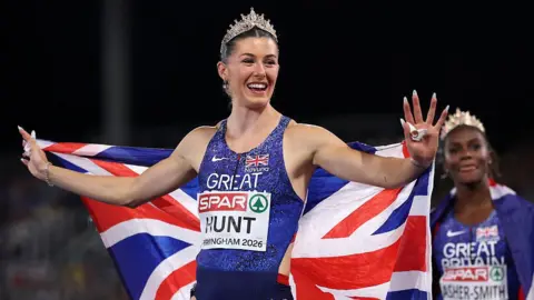 Getty Images Team GB's Amy Hunt carrying the UK flag and wearing a crown 
