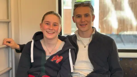 A teenage girl and boy sit together wearing grey tops