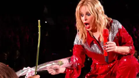 Kylie Minogue serenade leaves fan, 3, 'smiling ear to ear' 5 Glen Frost Kylie Minogue receiving a pink rose on stage in Birmingham with a shocked look on her face.