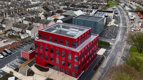 Aerial image of the new Innovation Centre. It is a large block building with red cladding with a small car park in the front. There is another modern office-type building next to it and the area is surrounded by terraced houses.