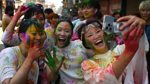 Getty Images Japanese tourists celebrate Holi, the Hindu spring festival of colours, along a road in New Delhi on March 14, 2025.