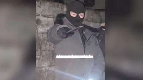 Counter Terrorism Policing Wales Alex Hutton wears a balaclava and poses with a machete