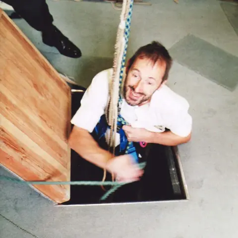 Mike Wigney Mike Wigney squeezing through a trap door in a bell tower to ring the bells.