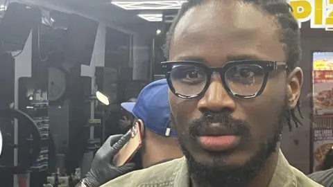 Chimbuomemma wearing a green jacket stood in a barbers shop after one of the group sessions 