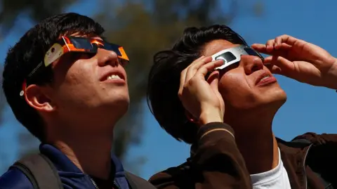 Two men look at the eclipse through special protective glasses