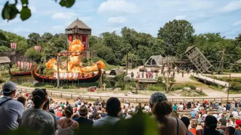 Puy du Fou A crowd sat watching a large Viking-based show at a Puy du Fou park. The scene is centred on a large Viking longboat which appears to be on fire.