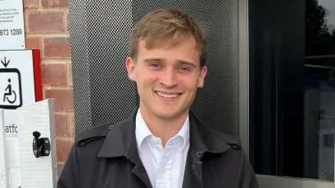 BBC/RICHARD EDWARDS Labour MP Keir Mather wearing a black rain coat and white shirt