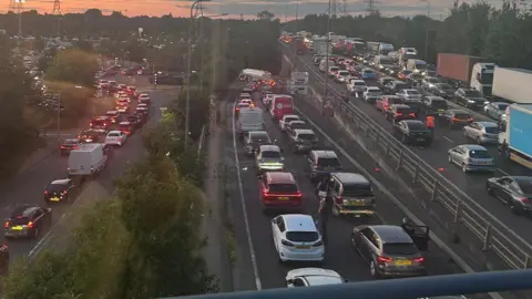 Eddy Keiller This picture taken from a bridge above a road shows three different roads, all dual-carriageway, gridlocked. Cars, vans and lorries are top to tail queuing during dusk. The queues are huge and cover the entire picture.