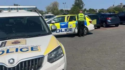 Dorset Police Two police cars and a male police officer. 