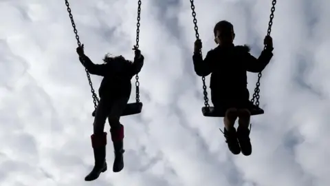 Two young children play on swings together.