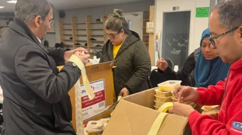 Islamic Society of Britain Two men and two women volunteers box up meals into boxes and put stickers on them