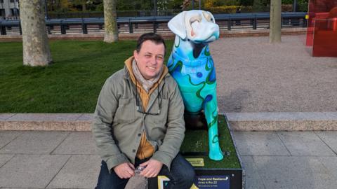 Kevin Gavaghan with the guide dog he designed, It is different shades of white and blue with vines going up its legs