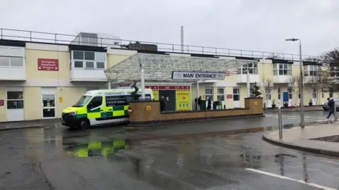 Frimley Park Hospital. A sign over a door says 'MAIN ENTRANCE.' An ambulance can also be seen.