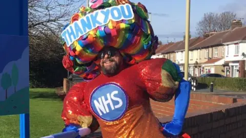 Colin Burgin-Plews Colin wearing a huge dress with NHS on it - and a headdress which says Thank you