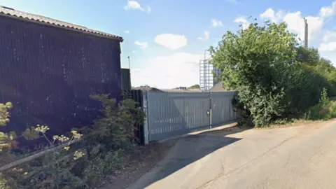 The gates of Hogwood Farm at Oxhill in south Warwickshire. They are wide aluminium gates leading to a silo on the right of picture with a low black-painted barn on the left.