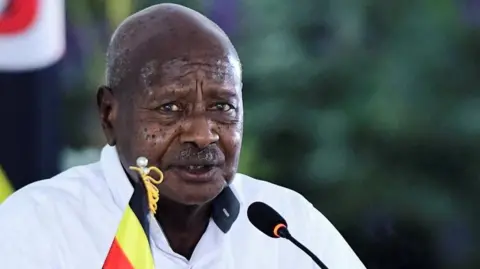 A head and shoulders image of Yoweri Museveni looking at the camera and speaking into a microphone.