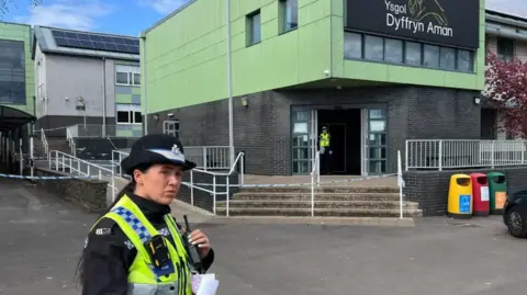 BBC A police officer stands outside the school in Ammanford