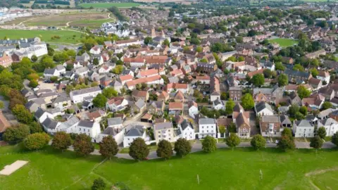 Getty Images An aerial view of part of Poundbury in 2022. Well-established trees in close proximity to each other line a road, which divides houses from an area of grass.