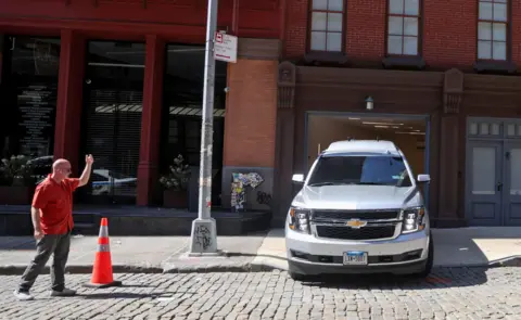Reuters A man stands on the street gesturing and waving while a grey Chevy SUV rolls out onto the street from a residential building in Manhattan.