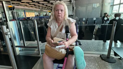 Amy Pohl Jo Pohl with sitting at the departure gates area of Heathrow with an annoyed expression