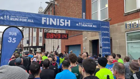 A crowd of runners going through a blue square arch with the word "finish" on.