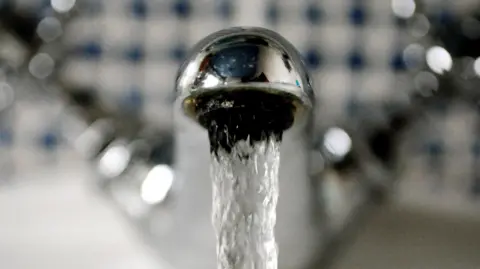 A silver tap with water running out of it in front of a blue and white tiled wall.