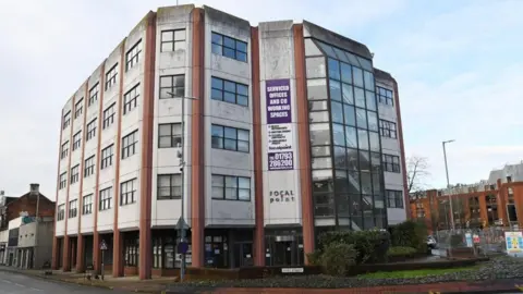 An exterior view of the focal point building, a grey concrete structure with red columns running down it along several points