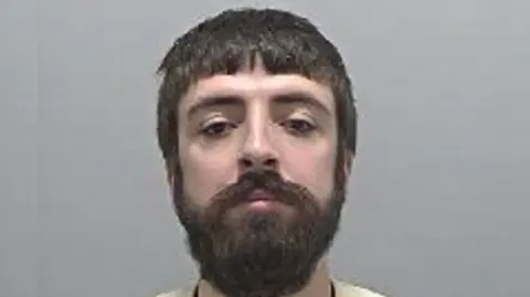 Hertfordshire Police A police custody image of Kyle Clifford, who has a thick dark beard and is standing against a grey backdrop