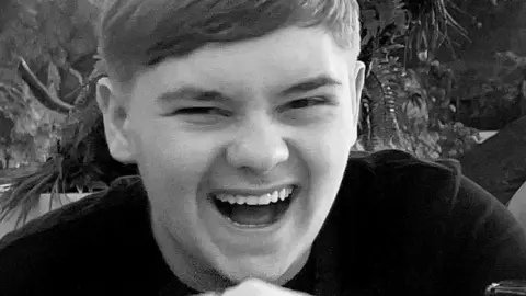 Black and white close-up of Harvey Willgoose, laughing and looking at the camera