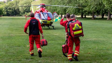 Thames valley air ambulance crew in all red uniforms walking on grass towards their red helicopter