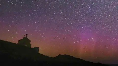 Northern Lights and a meteor over a rural skyline.