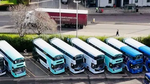 Several hydrogen buses lined up in parking bays, taken from the air.