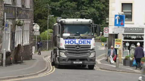 A heavy goods vehicle passes between two buildings on a narrow section of road in the town of Settle 
