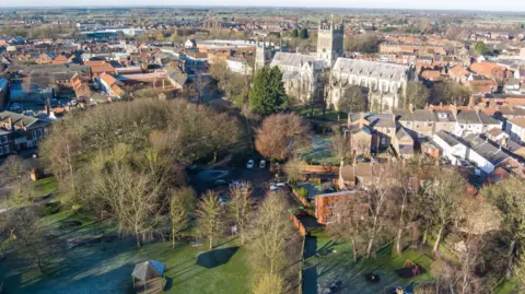 An aerial view of Selby Park, within which a bandstand and playground can be seen. In the background is Selby Abbey.