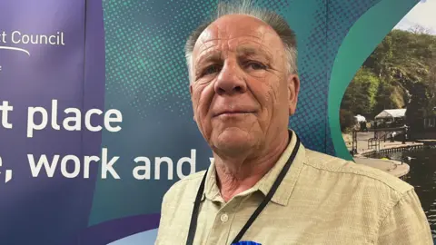 A man in a beige shirt looks at the camera