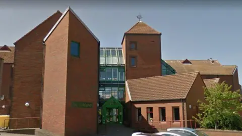 A brick fronted care home in the Borders with tall towers with few windows linked by a glass building with green frames
