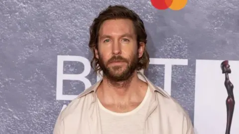 DJ Calvin Harris in a cream shirt and T-shirt with long hair and a beard