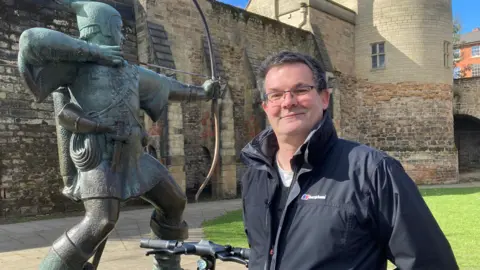 Tim Caswell from the company called Dott which is running the electric scooter scheme in Nottingham is standing near to the statue of Robin Hood outside Nottingham Castle where there is also one of the parking areas for scooters. 