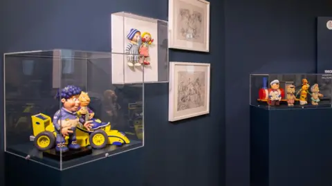 Jason Lock Props from various shows appear in glass display boxes attached to ble walls. Some pencil sketches have also been hung on the walls.