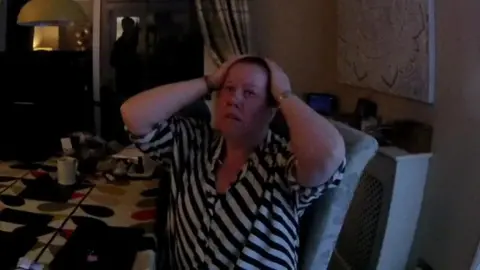 Crown Prosecution Service Michelle Mills is in a stripy black and white shirt. She is sitting at a table and has her hands on her head. 