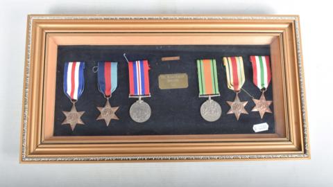 The six framed medals belonging to Cpl Kenneth Bateman have a variety of colours on their ribbons. Four of the medals are star shaped and two are silver circles.