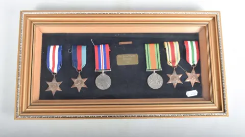 Richard Winterton Auctioneers The six framed medals belonging to Cpl Kenneth Bateman have a variety of colours on their ribbons. Four of the medals are star shaped and two are silver circles.