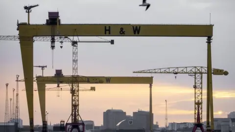 A wide shot of two yellow ship building cranes with the letters H&W in back bold writing.