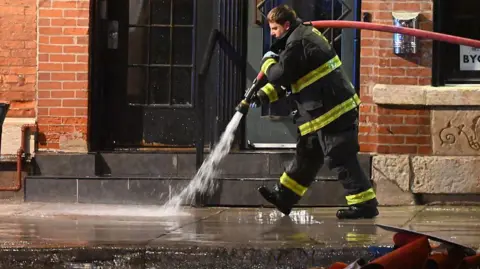 Male firefighter hosing down the pavement outside the nightclub
