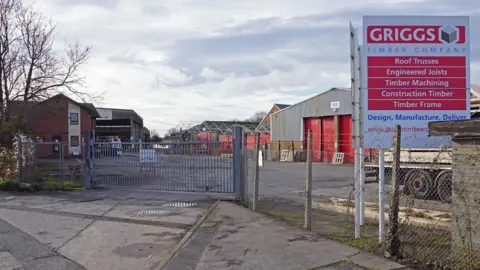 The Griggs building on an industrial estate, behind a metal gate. A red and white sign in the front says "Griggs Timber Company".