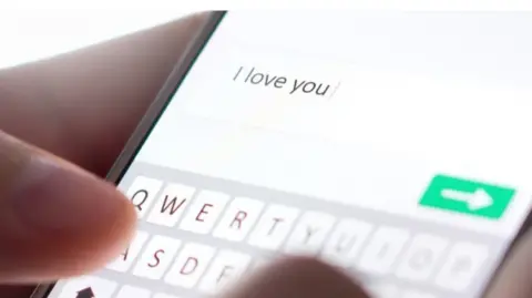 A phone screen with 'I love you' typed out on the screen. A hand appears to be holding the phone. 