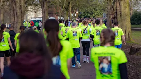 Wakefield Hospice A large group of runners jog through trees, wearing bright yellow T-shirts.