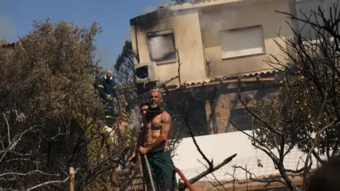 Residents assist firefighters in battling a wildfire burning in the coastal region of Palaia Fokaia, some 40km southeast of Athens